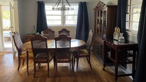 A dining room with a round table, six chairs, a chandelier, and a cabinet with glass doors. - Mountain Mama (Hendersonville)