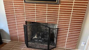 A fireplace with a decorative metal screen, set in a brick wall with a wooden floor. - Mountain Mama (Hendersonville)