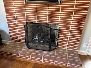 Un caminetto con una griglia metallica decorativa, incastonato in una parete di mattoni e con pavimento in legno.