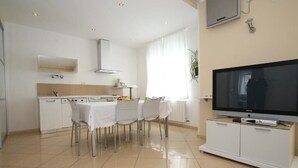 A modern kitchen with white cabinets, a dining table with chairs, and a flat-screen TV on a white cabinet. - Apartment  with a sea view (Baska)