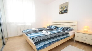 A bedroom with a bed, bedside tables, a radiator, a window with curtains, and a painting on the wall. - Apartment  with a sea view (Baska)