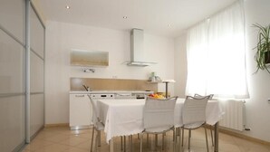 A modern kitchen with white cabinetry, a dining table set for four, and a window with sheer curtains. - Apartment  with a sea view (Baska)