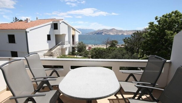 A balcony with a table and chairs overlooking a beach and mountains. - Apartment  with a sea view (Baska)