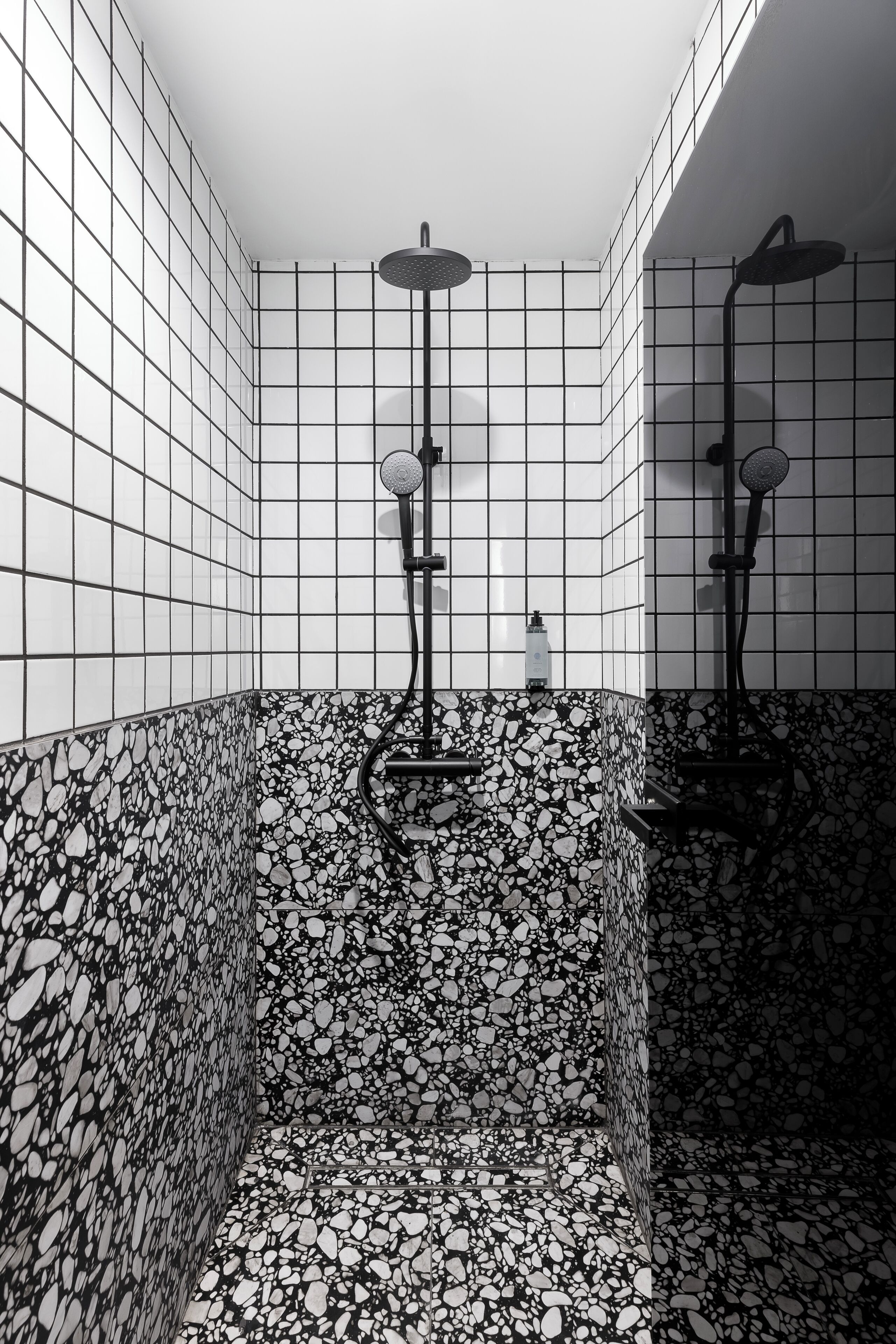 Et badeværelse med en flisebeklædt bruseområde, en marmorvæg og en shampoo på disken.