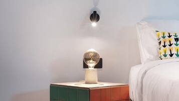A neatly arranged bedroom with a bed, a nightstand with a lamp, and a wall-mounted light fixture.