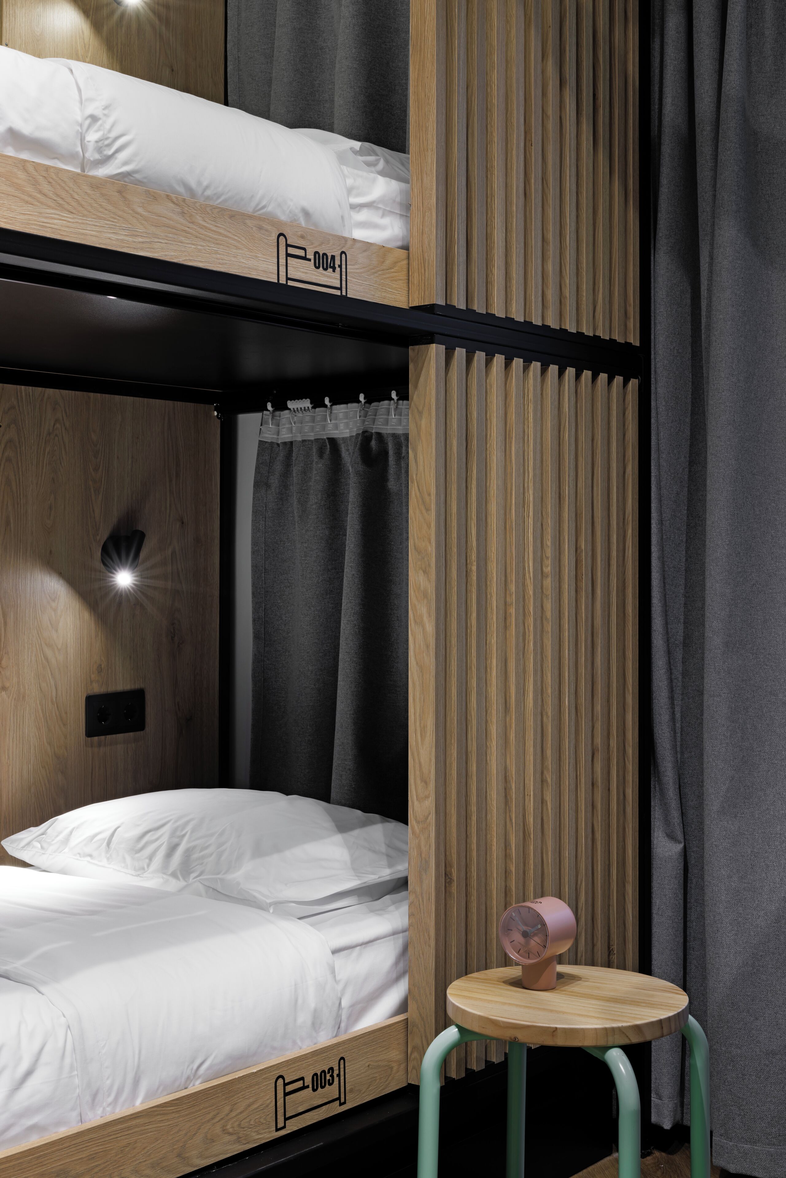 A bunk bed with a wooden headboard, a small round table with a clock, and a curtain.