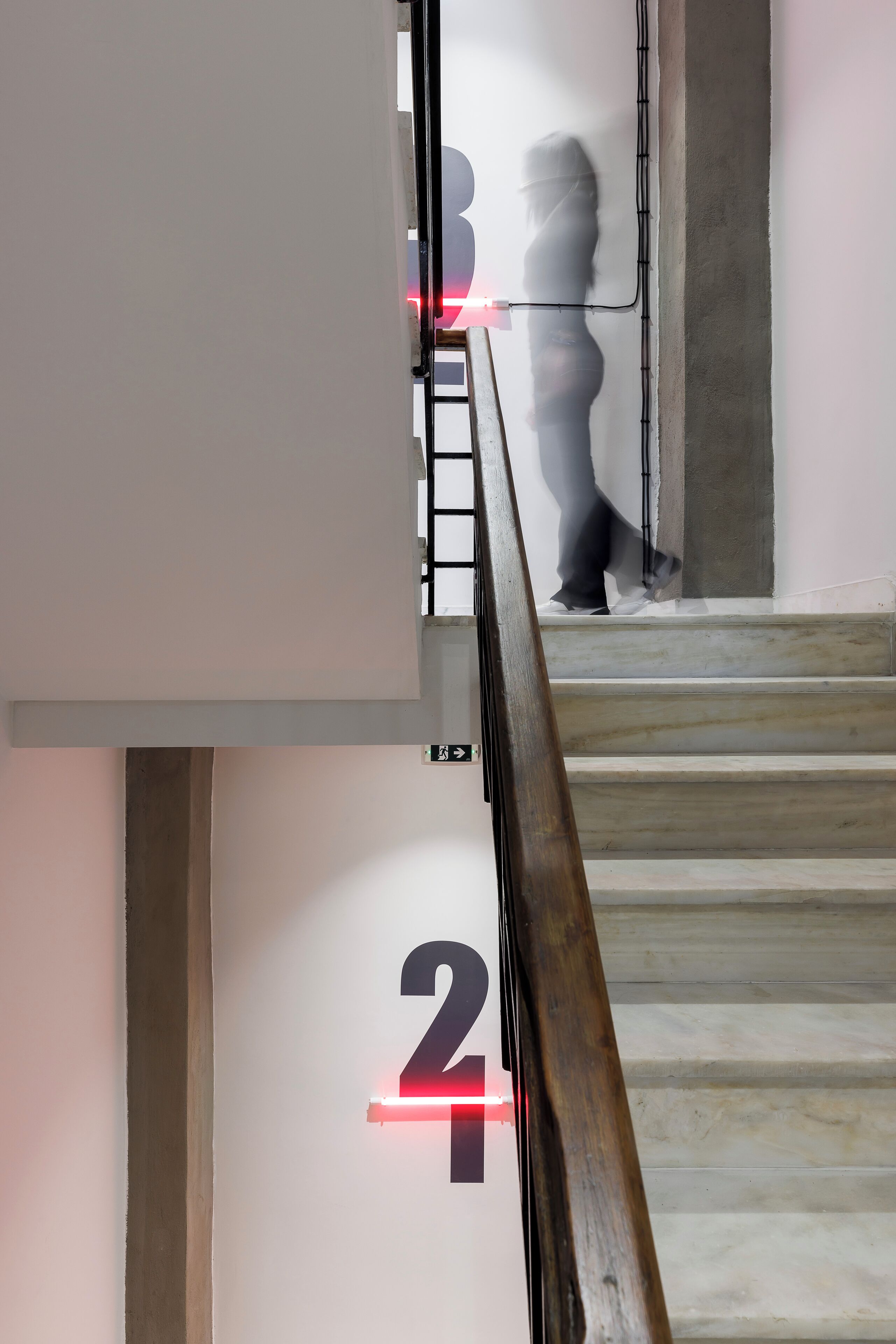 Una escalera con barandilla, una persona bajando y un letrero con el número 2 en la pared.