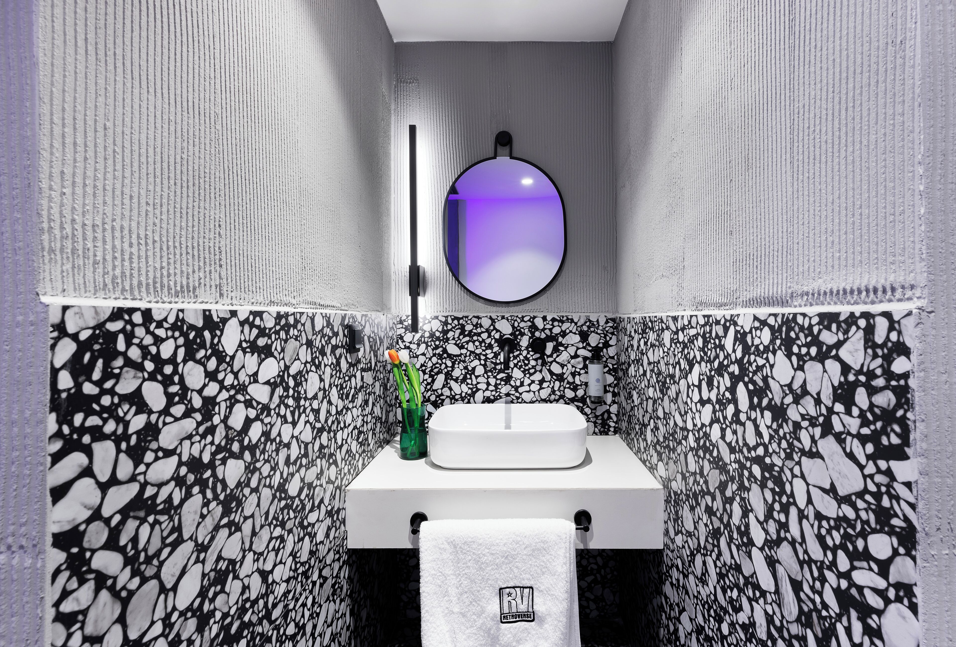 A bathroom with a white sink, a towel hanging on a rack, and a mirror with a purple reflection.