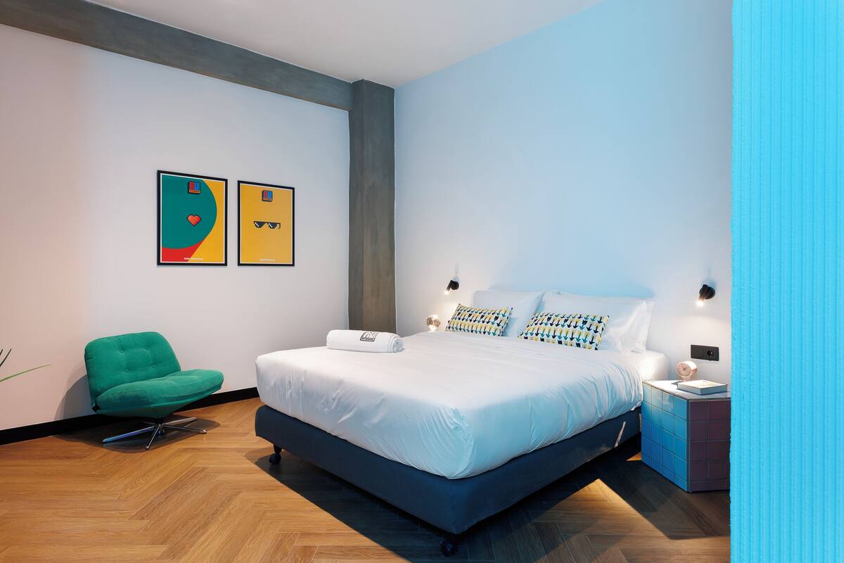 A modern bedroom with a large bed, a green chair, and two framed artworks on the wall.