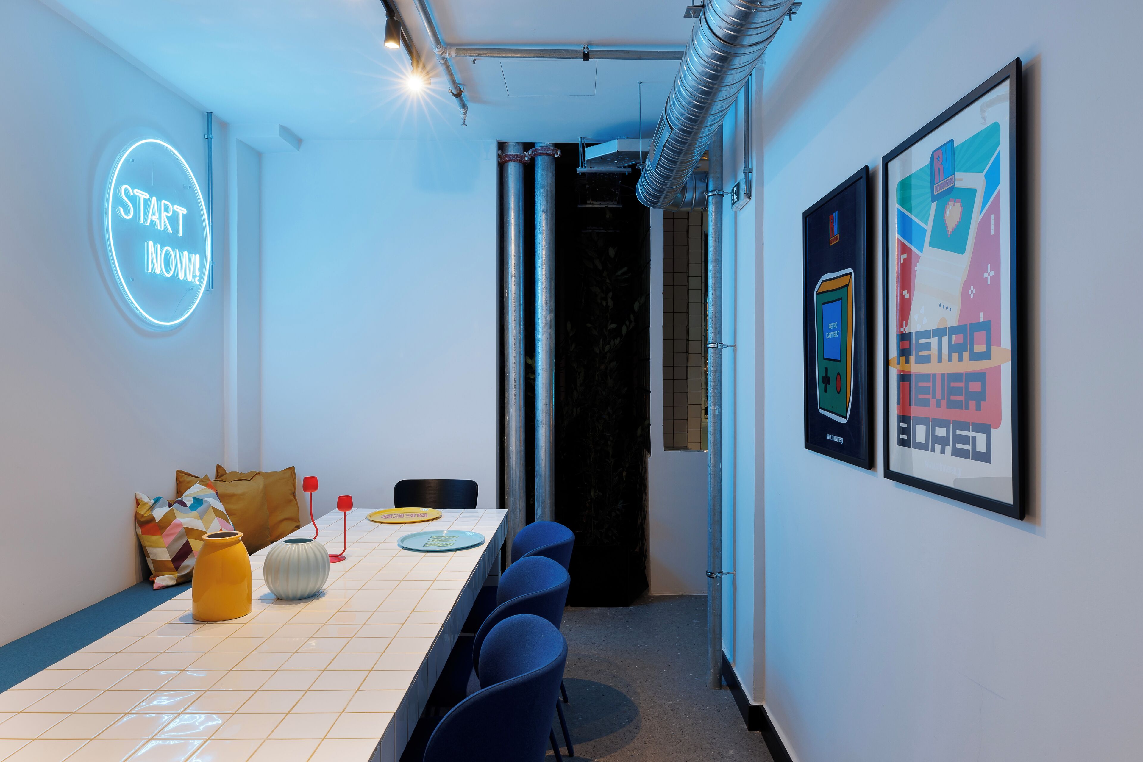 A conference room with a long table, chairs, a neon sign, and framed artwork on the wall.