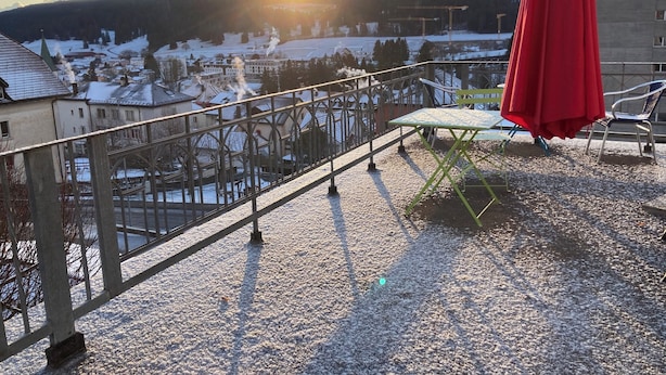 Ein Balkon mit Metallgeländer, einem roten Sonnenschirm und einem Tisch mit Stühlen.