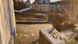 Ein verschneiter Innenhof mit einer Steinmauer, einem Holzbauten und Häusern im Hintergrund.