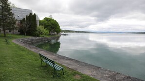 A calm lake with a stone walkway, a bench, and a building with a distinctive roof.