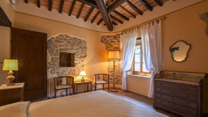 A bedroom with a stone wall, a bed, a dresser, two chairs, a lamp, and a window with curtains. - Villa in Cortona with 8 bedrooms sleeps 16 (Cortona)