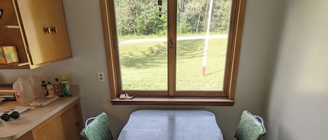 Un comedor con una mesa y sillas, un ventanal con vistas a una zona verde, armarios de madera y una lámpara en el techo.