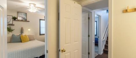 A hallway with a bed, a ceiling fan, and a staircase leading to another room.