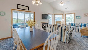A dining area with a table and chairs, a sofa set, a ceiling fan, and a television. - Oceanside 5BR pet-friendly Corolla home with private pool & hot tub! (Corolla)