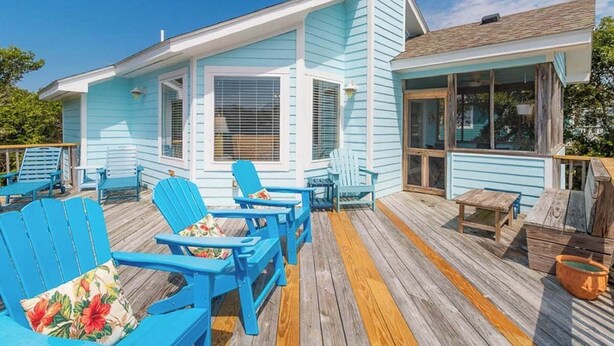 A light blue building with a covered deck, outdoor seating, and a large window. - Oceanside 5BR pet-friendly Corolla home with private pool & hot tub! (Corolla)