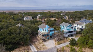 A coastal residential area with multiple houses, some with decks and balconies, surrounded by dense trees and a view of the ocean. - Oceanside 5BR pet-friendly Corolla home with private pool & hot tub! (Corolla)