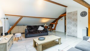 Un loft moderno con vigas de madera a la vista, un sofá de cuero oscuro, una mesa de centro de madera y un escritorio con lámpara.