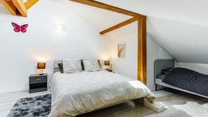 Un dormitorio con cama, mesitas de noche, una alfombra mullida, una viga de techo de madera y una lámpara fijada a la pared.