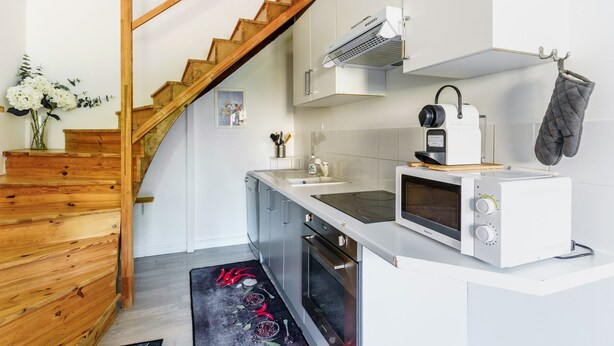 Una cocina moderna con escalera de madera, armarios blancos, un microondas y un lavabo.