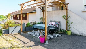 Un espacio de estar al aire libre cubierto con una pérgola de madera, una mesa con mantel azul y una silla.