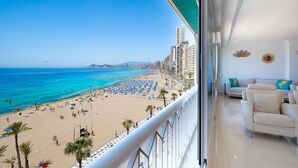 Un balcón con vista a una playa, un sofá y una pared decorada con hojas y un sombrero.