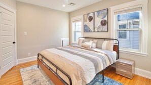 Un dormitorio con cama, mesitas de noche, ventilador de techo y una obra de arte en la pared.