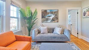 Una sala de estar con un sofá gris, un sillón naranja y una planta grande en maceta.