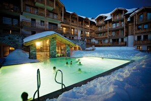 A heated outdoor swimming pool surrounded by snow, with wooden buildings in the background. - Wifi, ski-in/ski-out & foot of the slopes, view mountain, swimming pool, hammam, terrace, balcony (Montgenèvre)