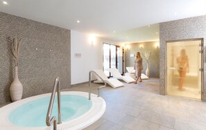 A spa area with a hot tub, lounge chairs, and a glass door.