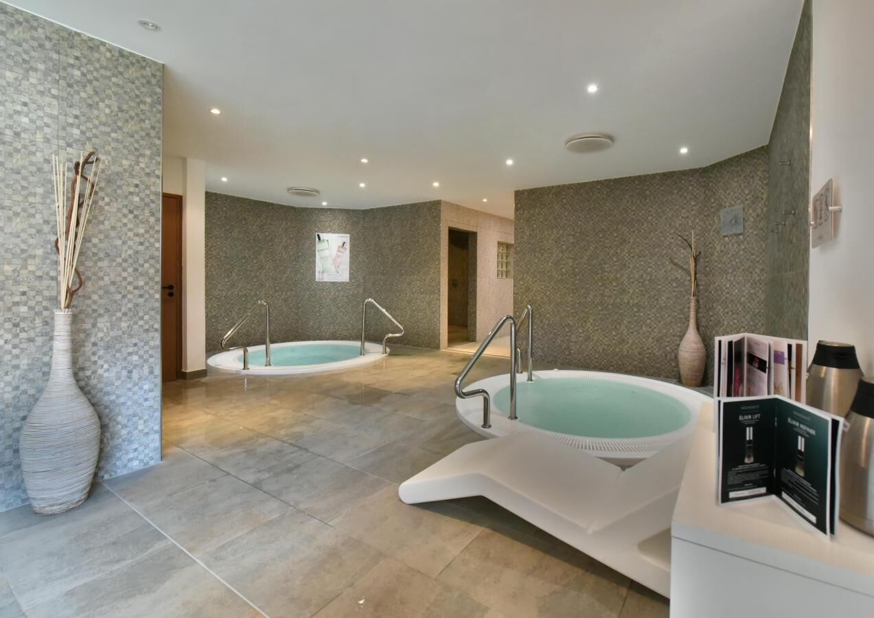 A modern spa area with two hot tubs, a reception desk, and a decorative vase.
