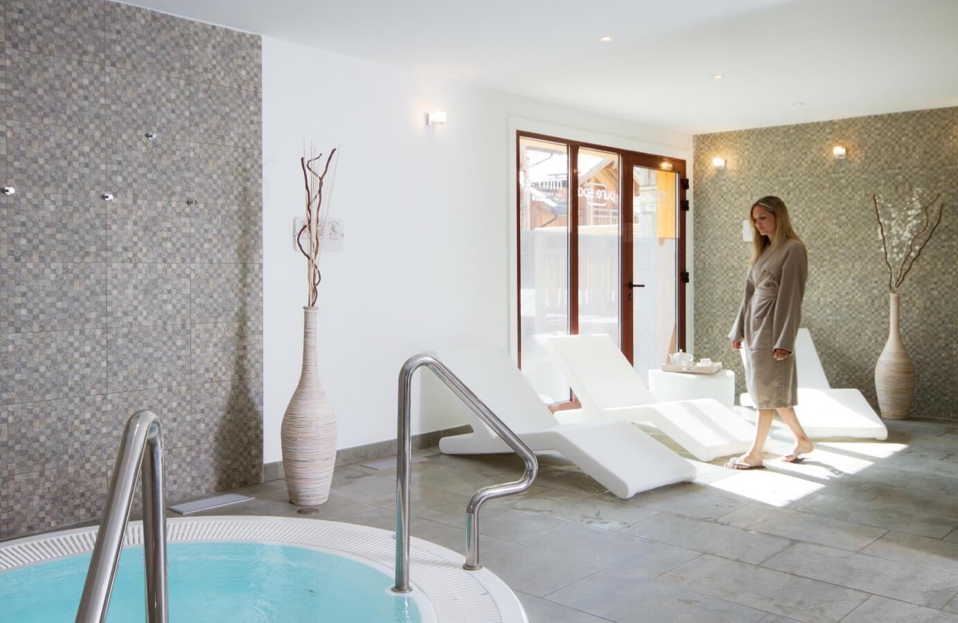 A modern indoor pool area with a clear pool, lounge chairs, and a large vase.