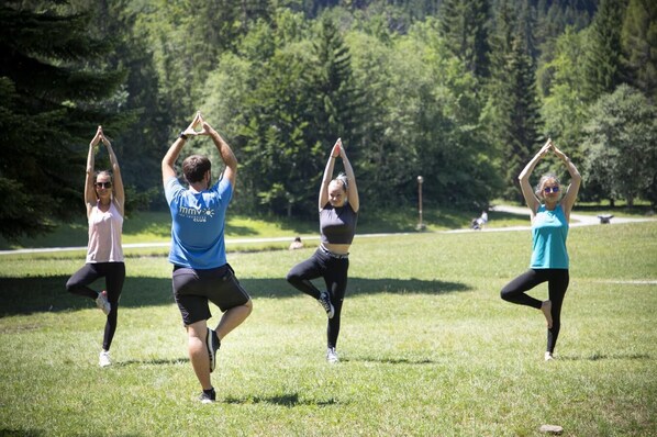Four people performing yoga in an outdoor grassy area with trees in the background.