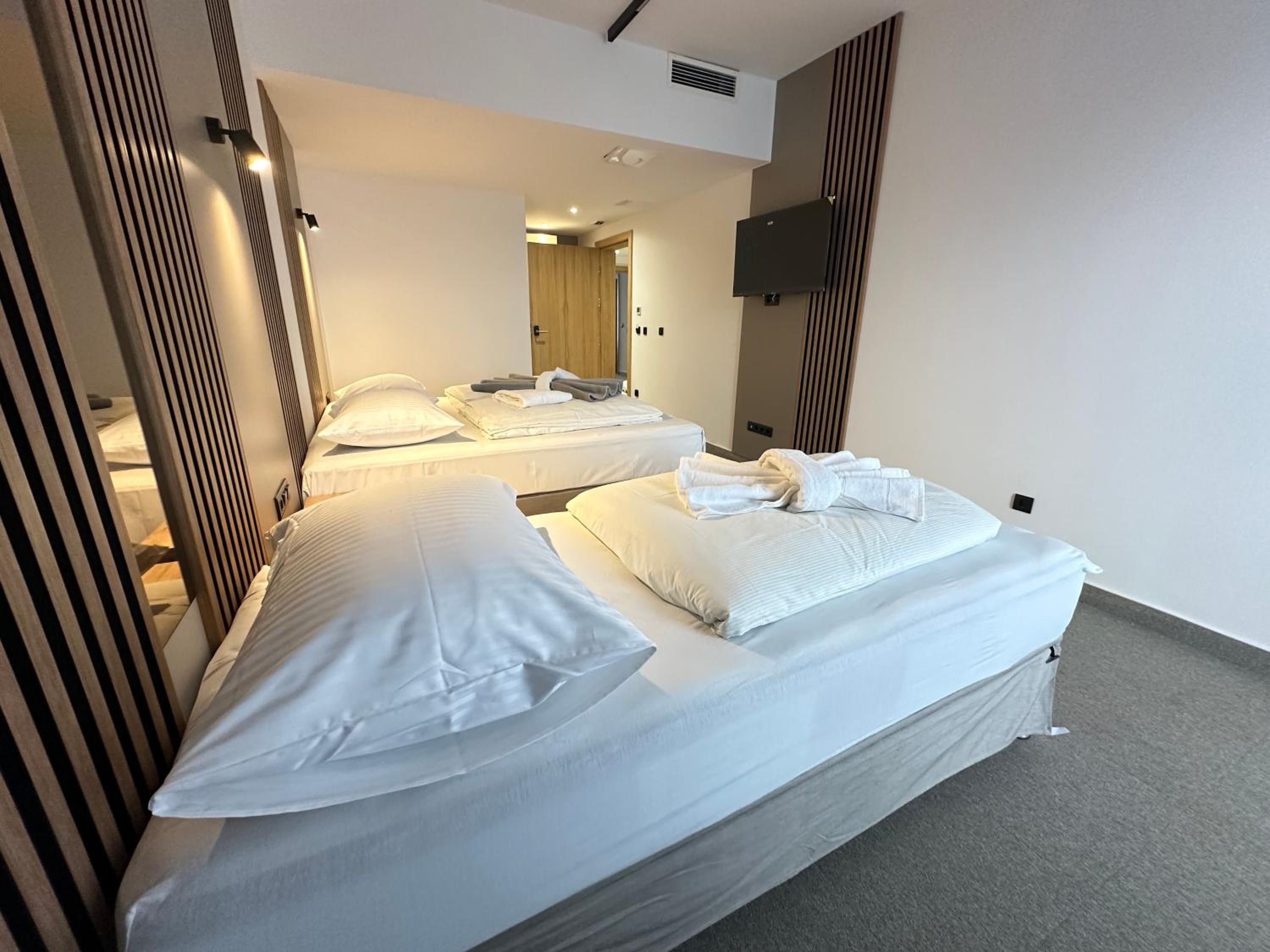 A hotel room with two beds, a flat-screen TV mounted on the wall, and a mirror reflecting the room.