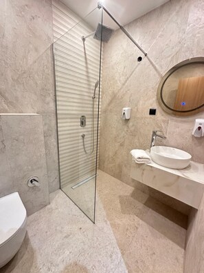 A modern bathroom with a glass-enclosed shower, a sink with a mirror, and a toilet. - Hotel Suljovic (Sarajevo)