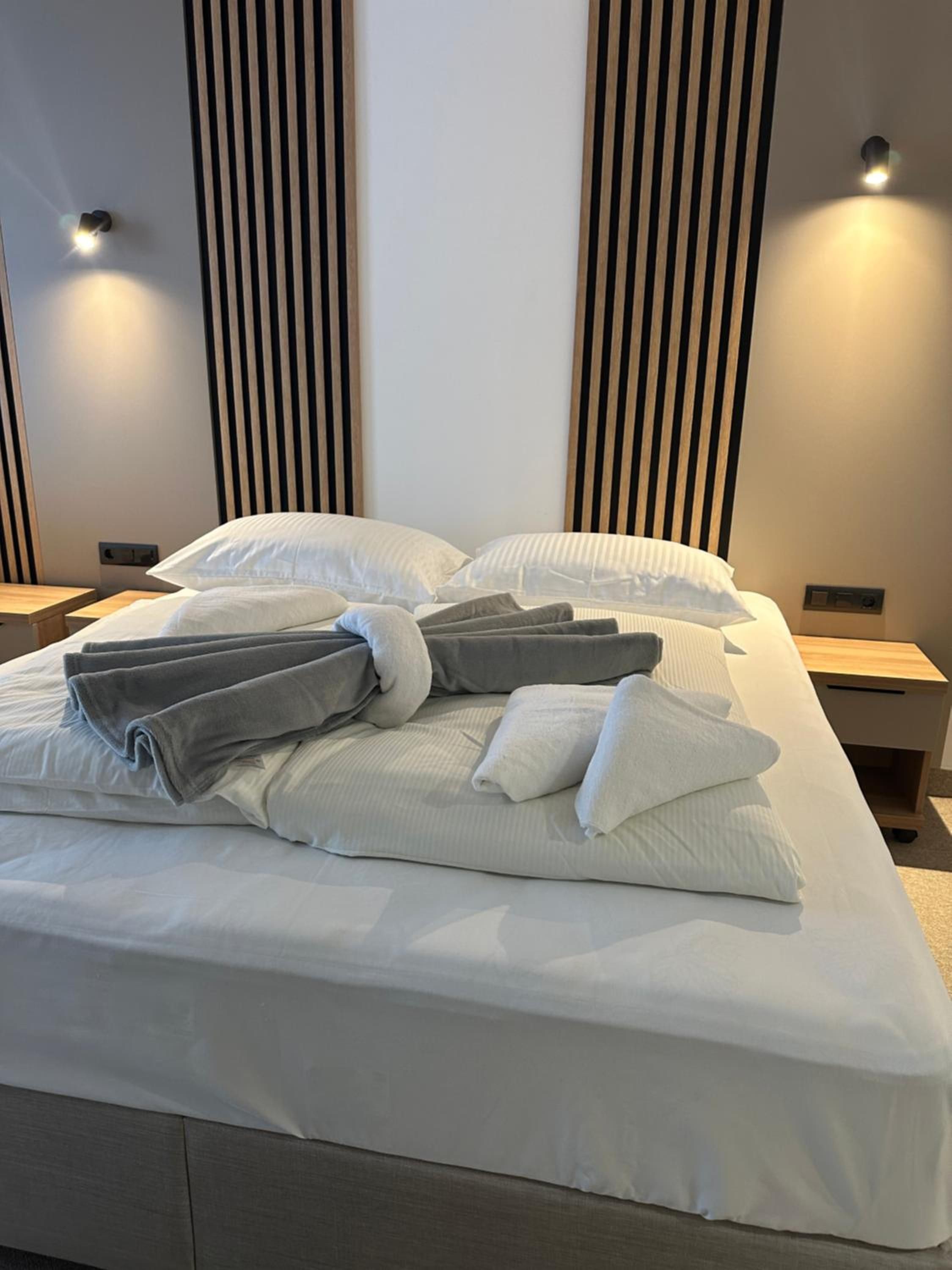 Un lit bien fait, avec des oreillers et des serviettes pliées, une table de chevet et un luminaire fixé au mur.