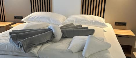 Un lit bien fait, avec des oreillers et des serviettes pliées, une table de chevet et un luminaire fixé au mur.