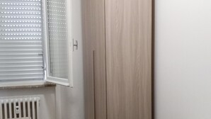 Ett sovrum med en säng, en garderob, ett element och ett fönster med persienner.