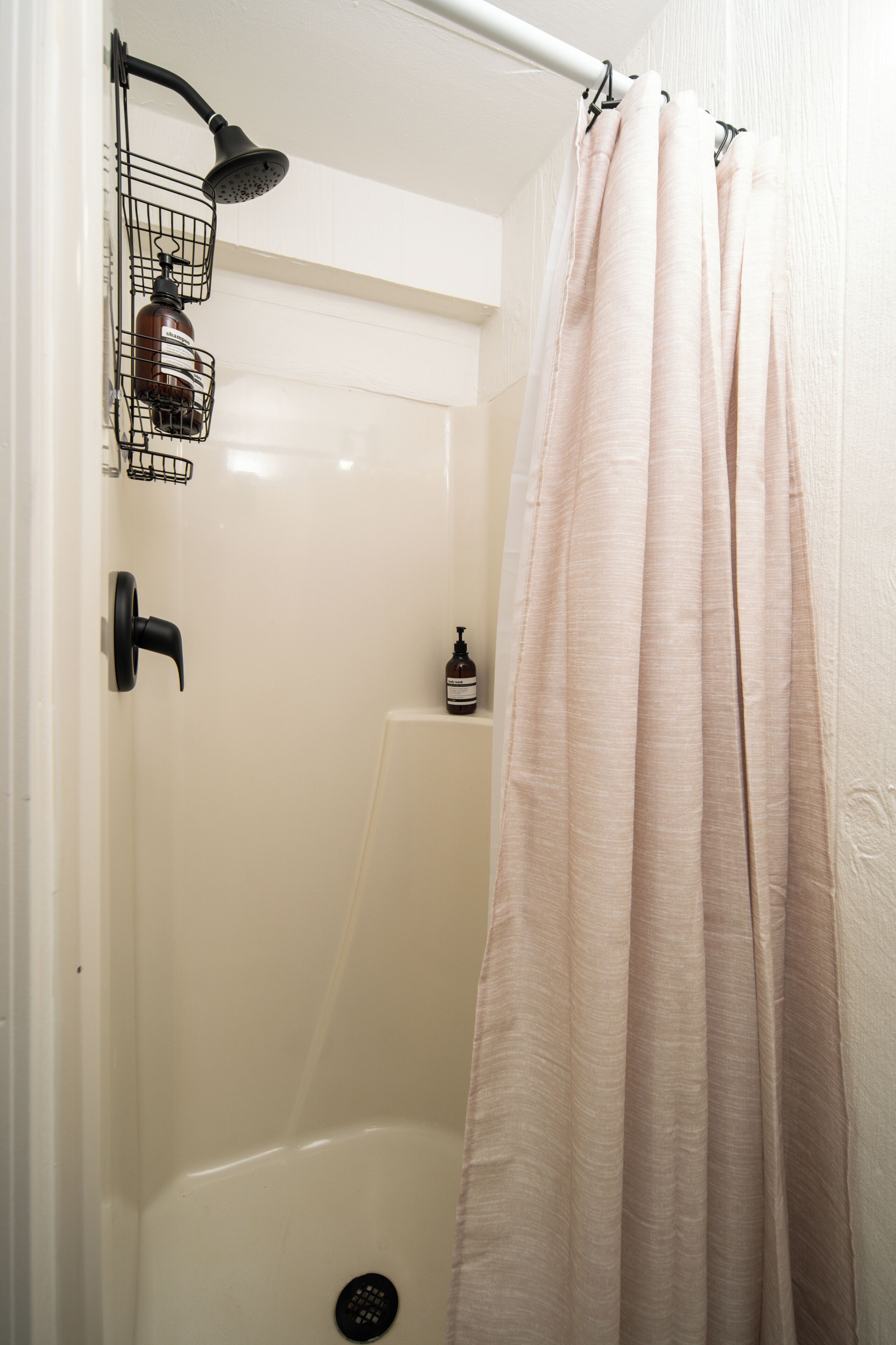 Un espace douche comprenant une baignoire blanche, une pomme de douche, un distributeur de savon et un rideau.