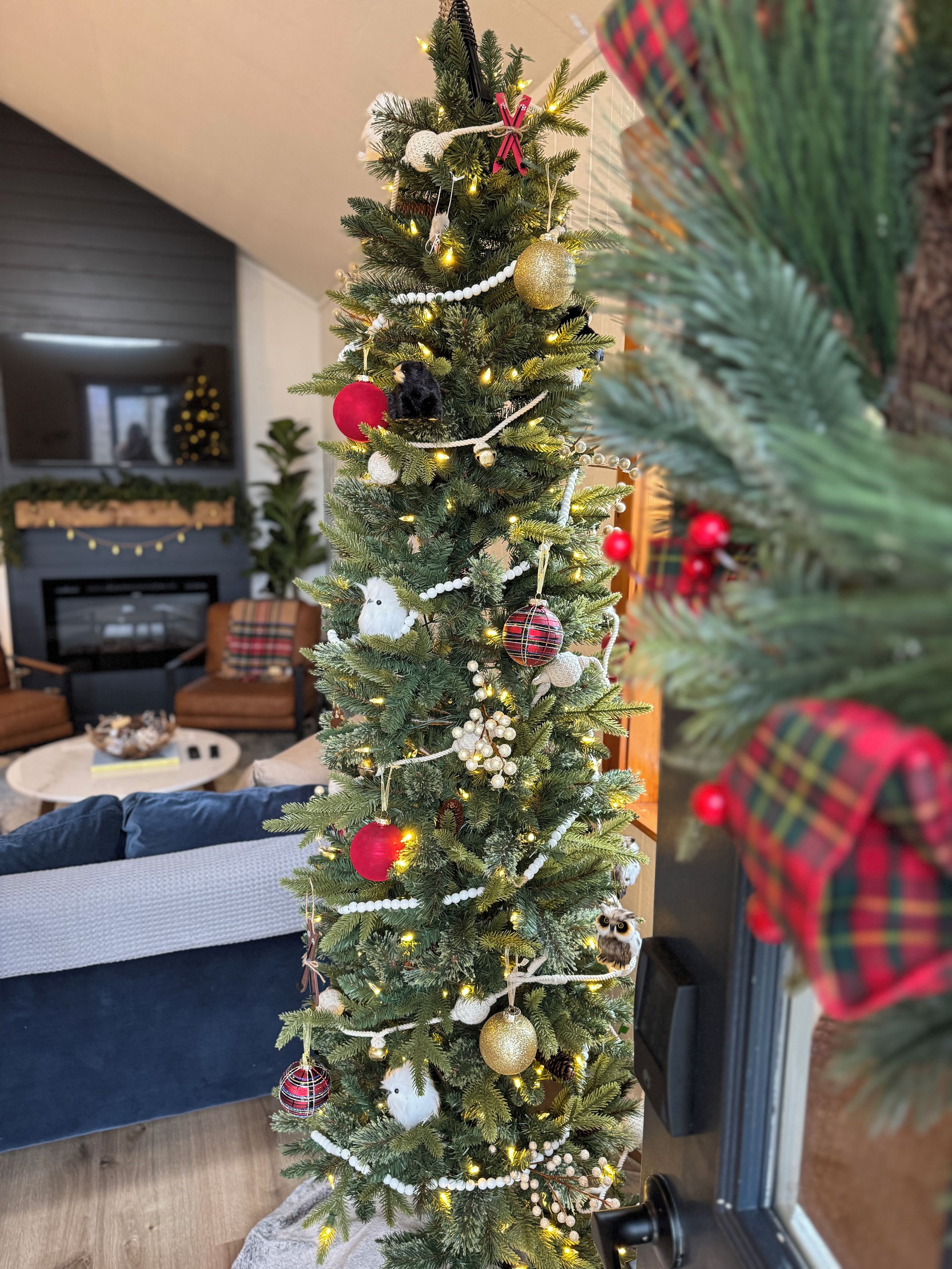 A decorated Christmas tree with ornaments and lights, situated in a living room with a fireplace and seating area.