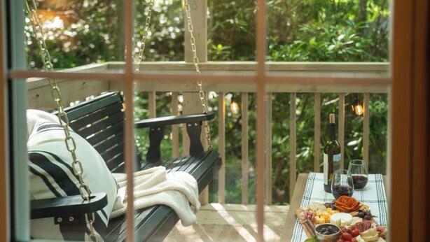Een houten bank met een kussen en een tafel met een kaasplank en wijnglazen.