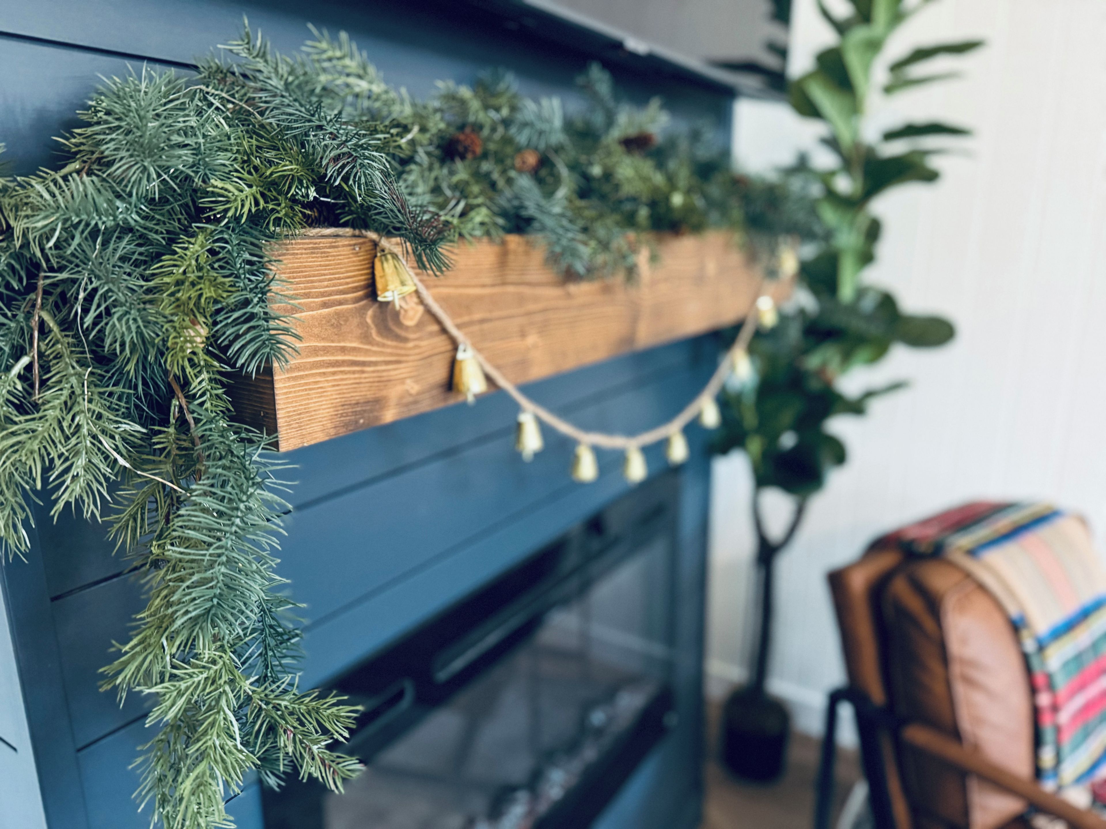 A fireplace with a wooden mantel decorated with greenery and string lights.