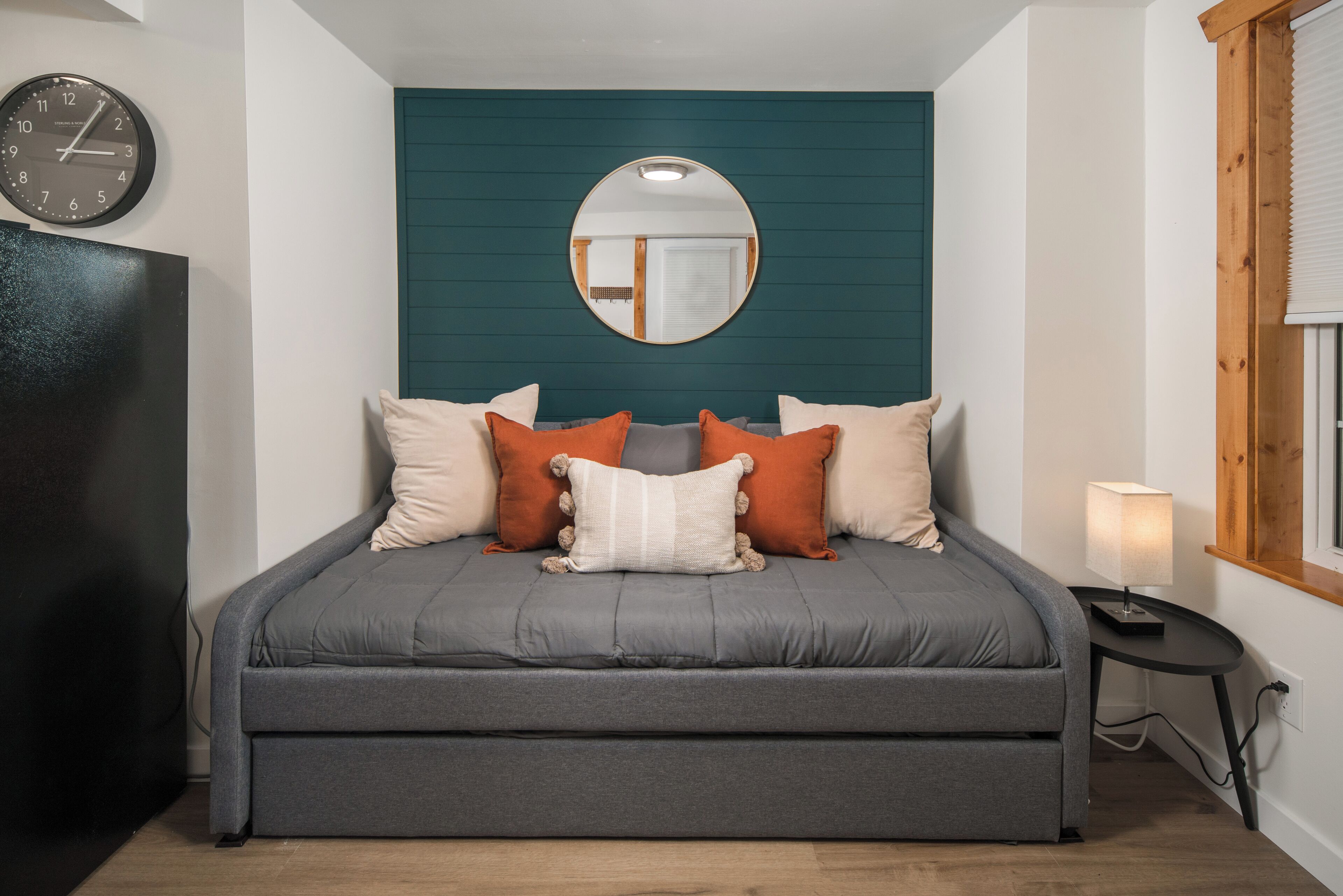 Une chambre à coucher avec un lit, une horloge, un miroir et une fenêtre.