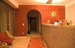 Un vestíbulo de hotel con suelo de baldosas, pared roja, mostrador de recepción y una silla.