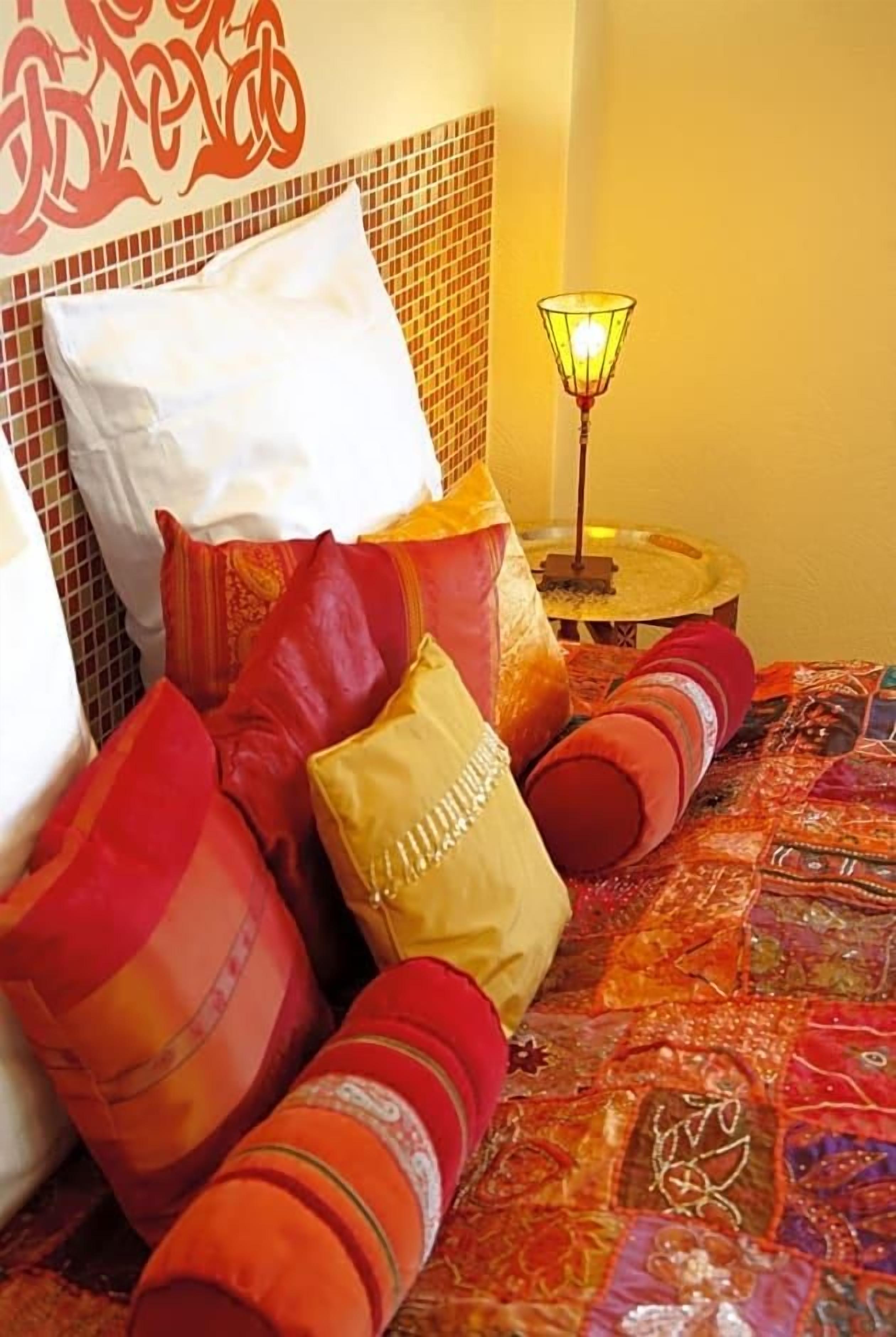 Ein Bett mit vielen Kissen, einer gemusterten Bettdecke und einer Wand mit dekorativem Fliesendesign.