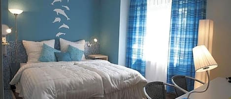 Un dormitorio con cama, una silla, una mesita de noche, una lámpara y una pared con siluetas de delfines.