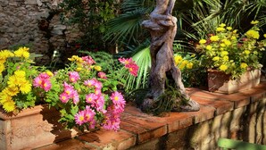 A garden with a wooden sculpture, various flowering plants, and a stone wall. - Chambres d'hôtes Peu del Causse SPA (Sainte-Colombe-de-la-Commanderie)