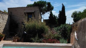 A hot tub in a garden with a stone wall, a small building, and trees. - Chambres d'hôtes Peu del Causse SPA (Sainte-Colombe-de-la-Commanderie)